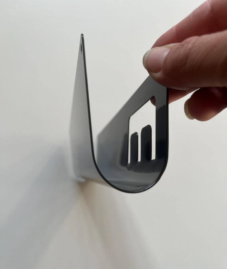 May include: A glossy black metal wall-mounted shelf with a curved, U-shaped profile. The side panel features a rectangular cutout with three vertical slats. A small circular mounting hole is visible at the top edge of the flat back section.