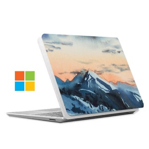 May include: A white laptop with a watercolour design of a mountain range at sunset. The design features a blue and white mountain range with a pink and orange sunset sky.