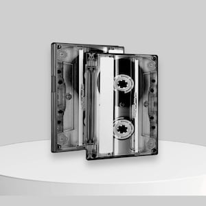 Può includere: Due cassette audio nere con custodie in plastica trasparente. Le cassette sono impilate l'una sull'altra. Le cassette hanno un'etichetta argentata con testo nero.