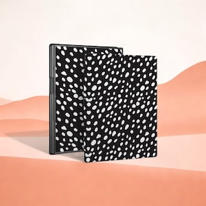 May include: Two black and white patterned phone cases with a white polka dot design on a black background. The cases are stacked on top of each other.