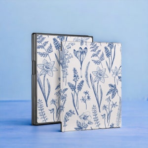 May include: Two book covers featuring a floral design. The covers are white with blue floral illustrations of daffodils, lilies, and other flowers. Both covers are closed and standing upright.