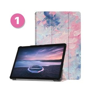 May include: A tablet computer with a black case and a screen displaying a photo of a boat on a beach at sunset. The tablet is next to a pink, blue and white patterned case.