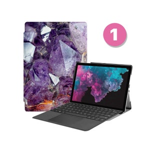 May include: A black laptop computer with a purple and blue abstract design on the screen. The laptop is closed and has a keyboard and trackpad. The laptop is sitting on a purple and white patterned case.