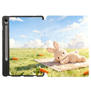 May include: Tablet case with a whimsical illustration of a plush bunny lying on a rug in a field with carrots. The background features a blue sky with fluffy clouds. The case is black.