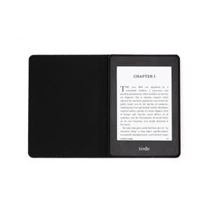 May include: A black Kindle e-reader with a black cover. The screen displays the text "CHAPTER I" and a passage from a book. The Kindle logo is visible at the bottom of the screen.