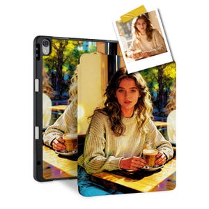 May include: Black iPad case featuring a digital art print of a woman in a cafe, holding a coffee. The case has a black frame with white accents. A small photo is taped to the case.