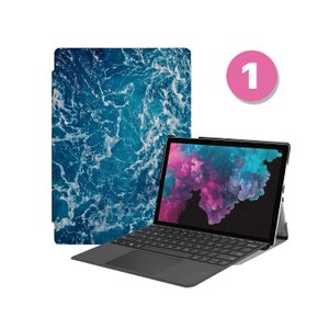 May include: A black laptop with a blue and white patterned case. The laptop is open and the screen shows a pink and blue abstract design. The laptop is on a white background.