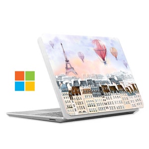 Könnte beinhalten: Ein weißer Laptop mit einem Aquarelldesign auf dem Deckel. Das Design zeigt den Eiffelturm, Heißluftballons und eine Stadtlandschaft.