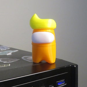 Könnte beinhalten: Orangefarbene und gelbe 3D-gedruckte Figur eines Charakters aus dem Videospiel Among Us. Der Charakter trägt einen gelben Hut und ein weißes Visier.