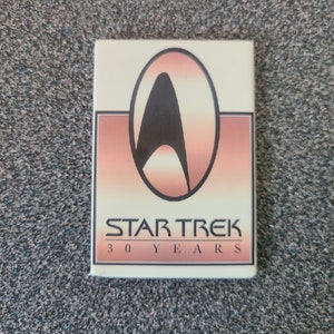 Könnte beinhalten: Ein weißer quadratischer Knopf mit rotem und orangefarbenem Hintergrund. Das Star Trek Logo befindet sich in der Mitte mit dem Text "STAR TREK 30 YEARS".
