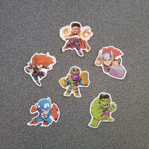 Può includere: Una collezione di sette adesivi in stile cartone animato con supereroi Marvel. Gli adesivi includono Captain America, Black Widow, Thor, Hulk, Thanos, Doctor Strange e Iron Man. Ogni personaggio è raffigurato in una posa dinamica.