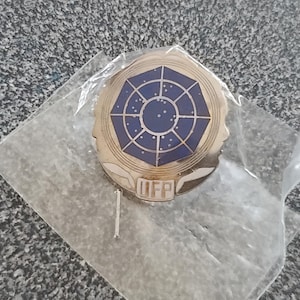 May include: A gold-colored pin with a blue and white star-shaped design. The pin has the text "UFP" in the center.