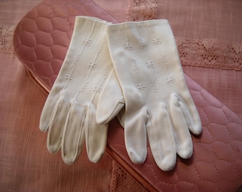 Puede incluir: Un par de guantes de algodón blanco con delicado bordado floral. Los guantes están sobre una superficie acolchada rosa.
