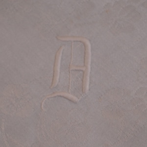 May include: White linen napkin with a white embroidered letter "D" in a script font.
