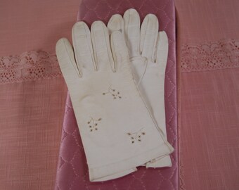 May include: A pair of white gloves with delicate floral embroidery on a pink quilted surface.