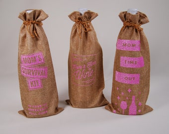Może przedstawiać: Trzy brązowe worki jutowe na butelki wina z różowymi błyszczącymi napisami. Worki są ozdobione tekstem "Mom's Survival Kit", "When's the last time I had wine?" i "Mom Time Out".