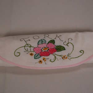 Puede incluir: Porta cubiertos de lino blanco con una flor bordada en rosa y verde y la palabra "FORKS" en cursiva.