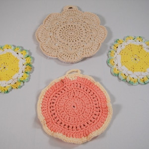 May include: Four crocheted pot holders in different colours and patterns. One is beige, one is yellow with a white and green border, one is pink with a white border, and one is yellow with a white and green border.