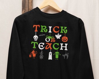 May include: Black sweatshirt with the text "Trick or Teach" in green, orange, and white. The text is surrounded by Halloween-themed icons, including a ghost, a skull, a spider, a pumpkin, a witch, a monster, and a cat.