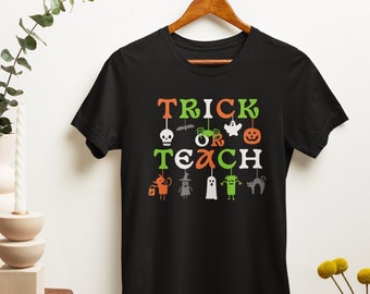 May include: Black t-shirt with the text "Trick or Teach" in white and green letters.  The text is surrounded by small Halloween-themed graphics, including a ghost, a spider, a skull, a pumpkin, and a bat.