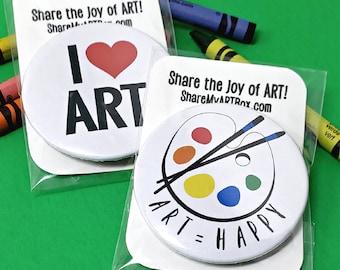 Puede incluir: Dos botones redondos blancos con texto negro e imágenes. El primer botón dice "¡Me encanta el ARTE!" con un corazón rojo. El segundo botón tiene una imagen en blanco y negro de una paleta de pintura con pinceles y el texto "ARTE = FELIZ".