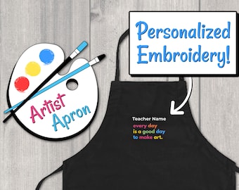 Puede incluir: Delantal negro de artista con un diseño de paleta de pintura y pinceles. El delantal tiene el texto "Artist Apron". El delantal también tiene el texto "Teacher Name every day is a good day to make art." bordado en colores arcoíris.