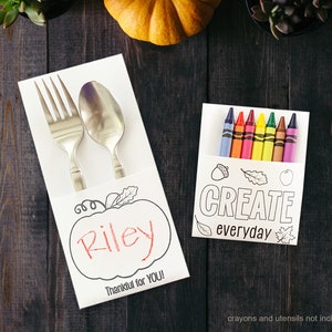 Pu&ograve; includere: Una tovaglietta di carta bianca con un disegno di zucca e il nome "Riley" scritto all'interno. La tovaglietta comprende una forchetta e un cucchiaio e il testo "Thankful for YOU!" in basso. Un biglietto di carta bianca separato con un disegno di zucca, ghianda e foglia include il testo "CREATE everyday" e una fila di otto pastelli.