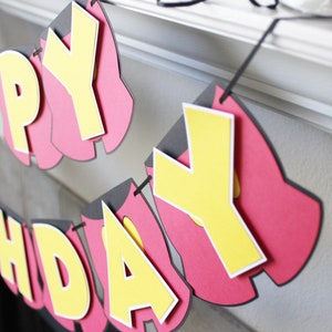 May include: A red and yellow paper banner with the words "Happy Birthday" hanging from a white surface.