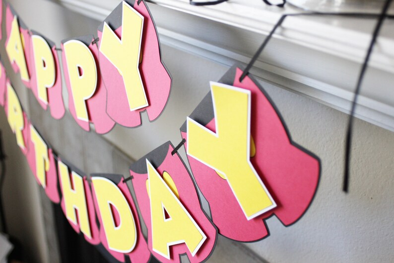 May include: A red and yellow paper banner with the words "Happy Birthday" hanging from a white surface.