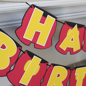 May include: A red and yellow banner with the words "Happy Birthday" in a Mickey Mouse-inspired font.