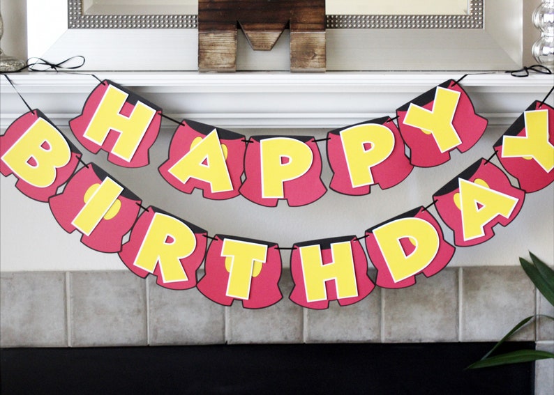 May include: A red and yellow birthday banner with the words "Happy Birthday" in a Mickey Mouse-inspired font. Each letter is shaped like Mickey Mouse's shorts.