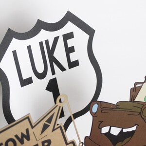 Może przedstawiać: Czarno-biały znak drogowy z napisem "LUKE" i numerem "1". Znak ma kształt tarczy. Na tle znajduje się brązowa kresk&oacute;wkowa ciężar&oacute;wka holownicza.