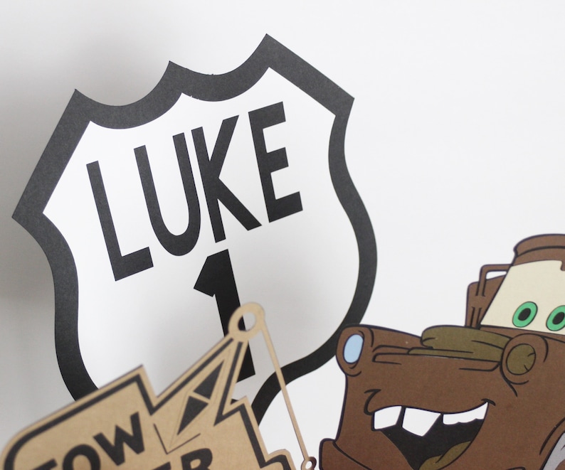 Może przedstawiać: Czarno-biały znak drogowy z napisem "LUKE" i numerem "1". Znak ma kształt tarczy. Na tle znajduje się brązowa kresk&oacute;wkowa ciężar&oacute;wka holownicza.