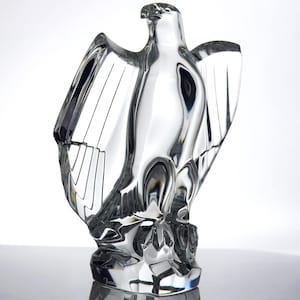 May include: A clear crystal eagle sculpture with outstretched wings. The eagle is perched on a textured base, with detailed feathering visible on the wings. The sculpture is highly reflective, catching the light.