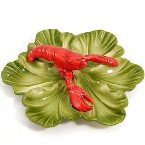 May include: A ceramic serving dish featuring a bright red lobster atop a large, green lettuce leaf design. The dish is likely used for serving appetizers or seafood dishes. The lobster has detailed claws and antennae.