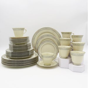 Könnte beinhalten: Ein Set aus elfenbeinfarbenem Porzellan-Geschirr mit einem zarten Blumenmuster in Rosa- und Grüntönen. Das Set enthält Teller, Schalen und Tassen.