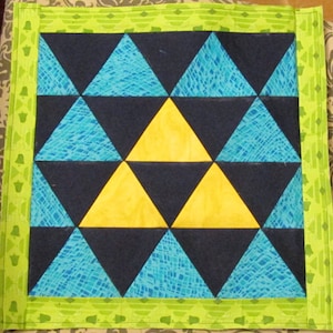 May include: A green and yellow quilted throw pillow with a geometric pattern of triangles. The triangles are in shades of blue, yellow, and black.