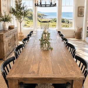 May include: A long rectangular wooden dining table with a natural brown finish and thick turned legs, surrounded by twelve black spindle-back chairs. A green garland and white pillar candles sit in the center of the table surface.