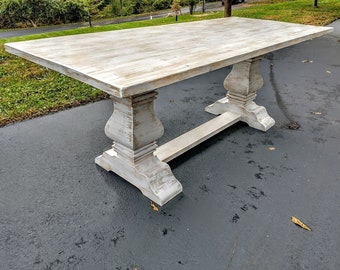 May include: White farmhouse style dining table with a distressed finish and a trestle base. The table has a rectangular top and is made of wood.