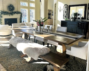 May include: A large wooden dining table with a white fur bench and chairs. The table is set with a black runner and a vase of flowers. A black cat is lying under the bench.