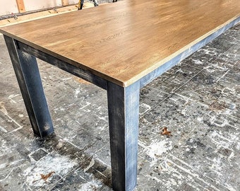May include: A large, rectangular wooden table with a light brown wood top and dark gray painted legs. The table is sitting on a concrete floor.