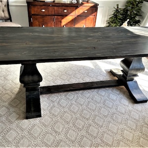 May include: A dark stained wood dining table with a rectangular top and a trestle base. The table is sitting on a white rug with a diamond pattern.