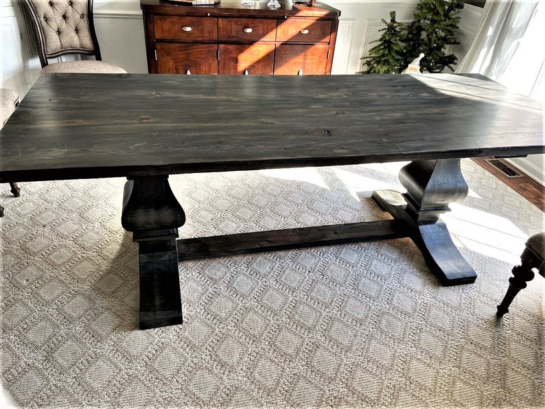 May include: A dark stained wood dining table with a rectangular top and a trestle base. The table is sitting on a white rug with a diamond pattern.