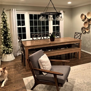 Puede incluir: Una mesa de comedor de madera con un banco y sillas, ubicada en una habitaci&oacute;n con un &aacute;rbol de Navidad, una l&aacute;mpara de ara&ntilde;a y una alfombra. La mesa tiene un acabado r&uacute;stico y est&aacute; rodeada de sillas con respaldos tejidos.