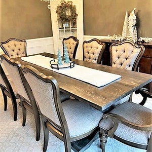 May include: A dining room set featuring a large, rectangular wooden table with eight upholstered chairs. The chairs have a tufted back design. A white table runner and decorative accents adorn the table, creating an elegant and inviting atmosphere. A chandelier hangs above.