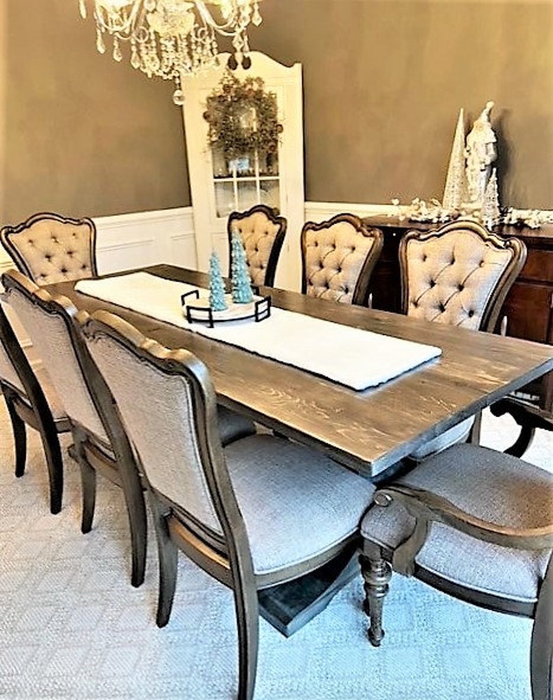 May include: A dining room set featuring a large, rectangular wooden table with eight upholstered chairs. The chairs have a tufted back design. A white table runner and decorative accents adorn the table, creating an elegant and inviting atmosphere. A chandelier hangs above.