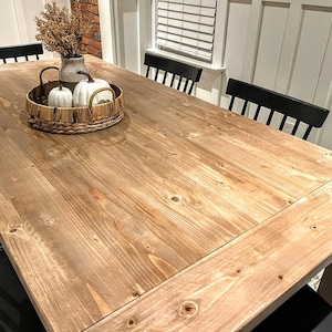 Puede incluir: Una mesa de comedor de madera clara con un acabado natural. La mesa tiene una tapa rectangular y un dise&ntilde;o sencillo. La mesa est&aacute; rodeada de sillas negras.