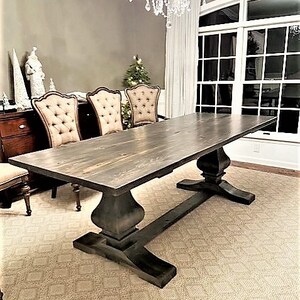 May include: A dark stained wood dining table with a trestle base and a rectangular top. The table is set in a dining room with a rug and chairs.