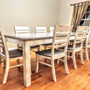 Puede incluir: Una mesa de comedor de madera blanqueada con seis sillas. La mesa tiene un acabado desgastado y las sillas tienen un respaldo de listones.