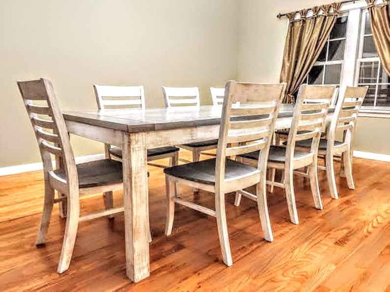 Puede incluir: Una mesa de comedor de madera blanqueada con seis sillas. La mesa tiene un acabado desgastado y las sillas tienen un respaldo de listones.